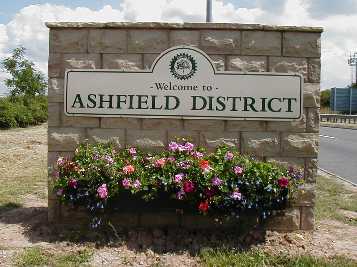 Image of a sign on a wall with flowers at its base that says Welcome to Ashfield District